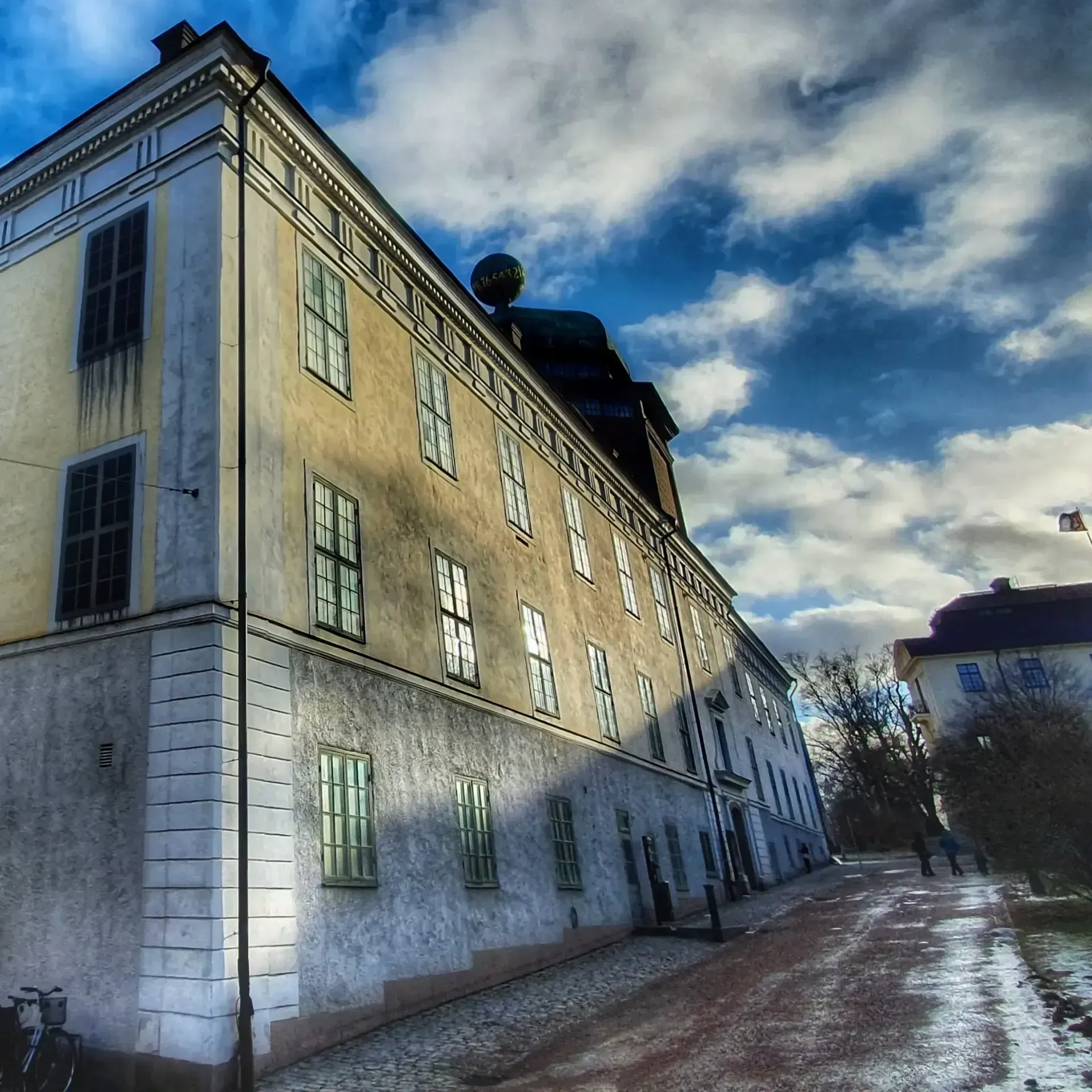 Gammal byggnad med många fönster, sedd från gatan. Blå himmel med moln. Stadsvandring Uppsala