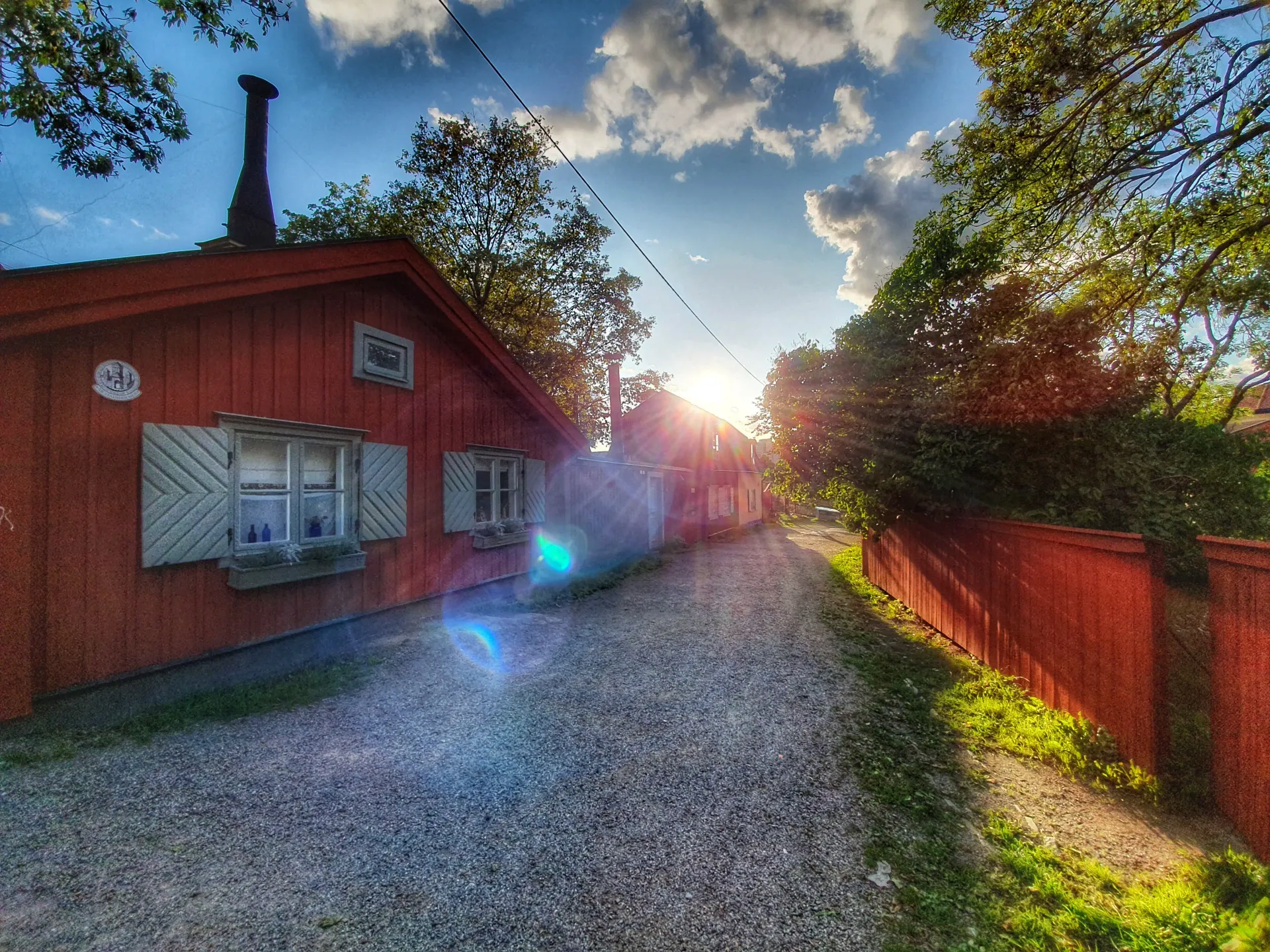 Röd träbyggnad och grusgång med sol och träd