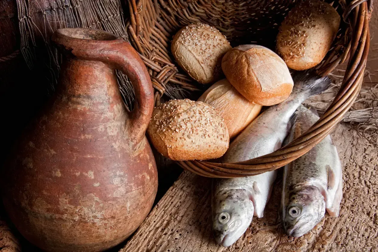 Stilleben med lerkruka, bröd och fisk i en flätad korg på ett träbord