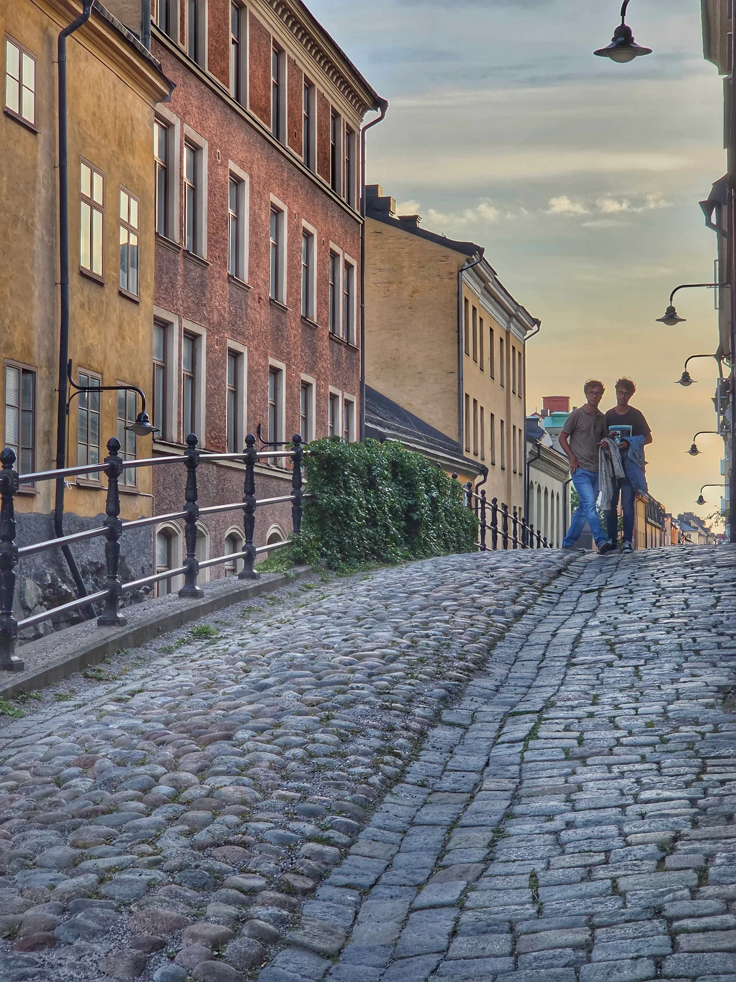 Två män på en stadsvandring i Mariaberget, går uppför brant kullerstensgata med gamla hus längs sidorna