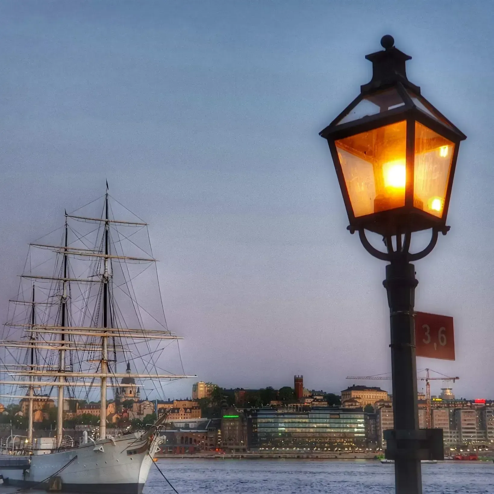 Lysande gatlykta, skepp och stadsbild vid vatten