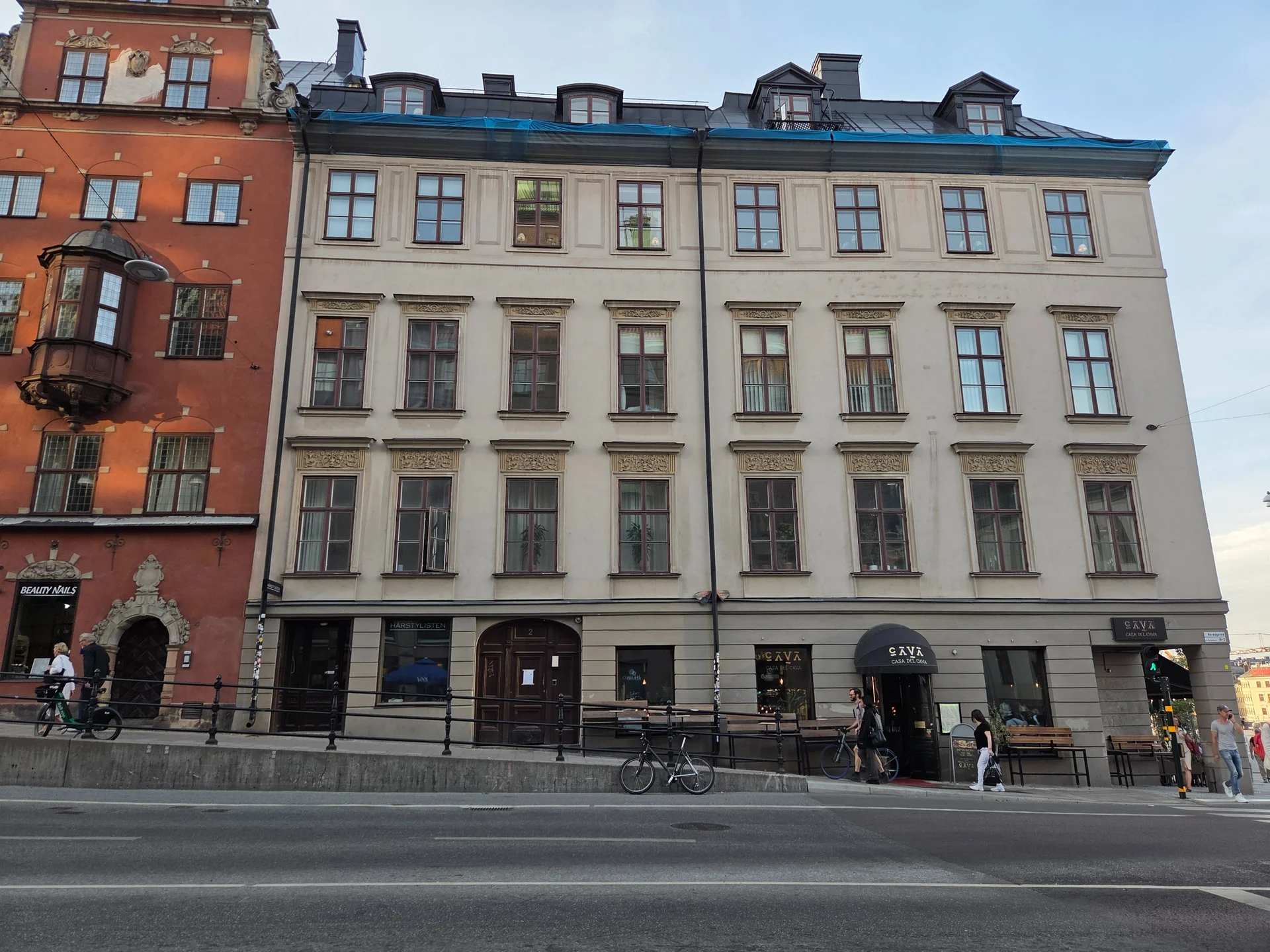 Byggnader på Mariaberget. Röd och ljus fasad med många fönster. Butiker och restauranger på gatuplan, människor promenerar