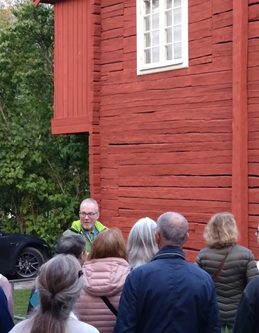 Grupp människor framför en röd träbyggnad med ett vitt fönster