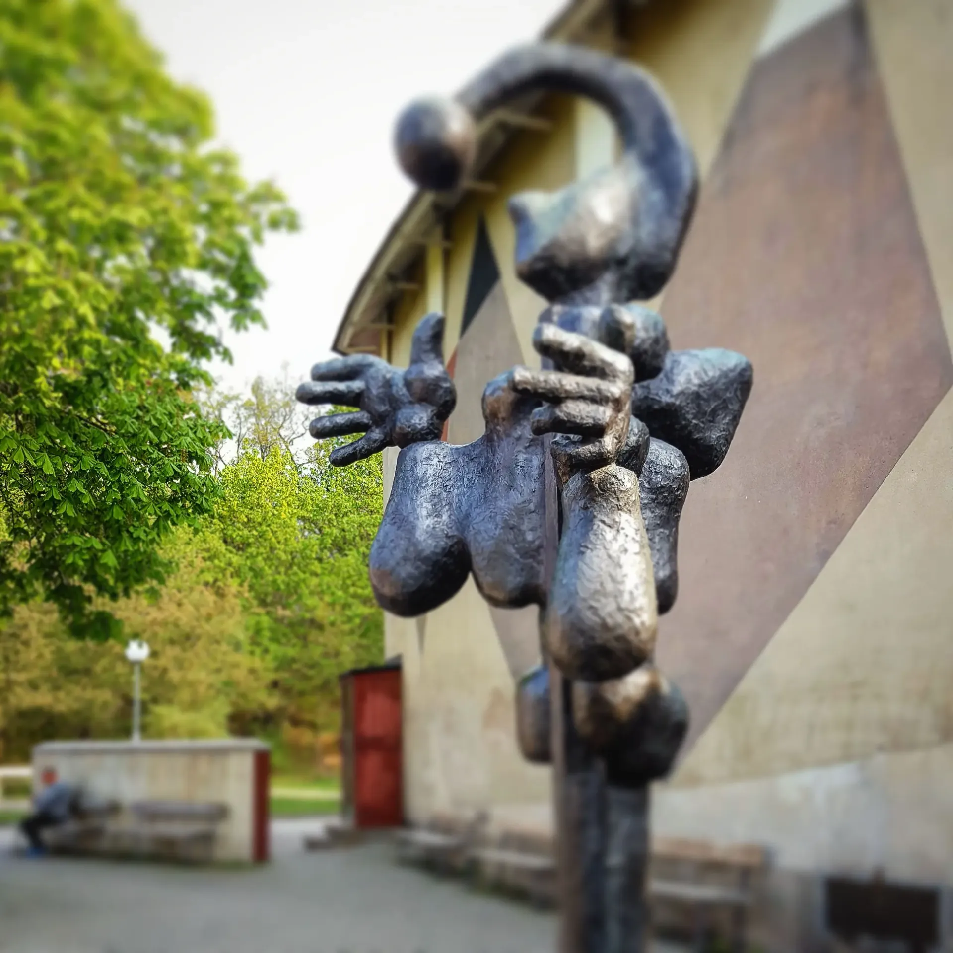 Abstrakt skulptur av metall utomhus. Byggnad i bakgrunden. Träd till vänster