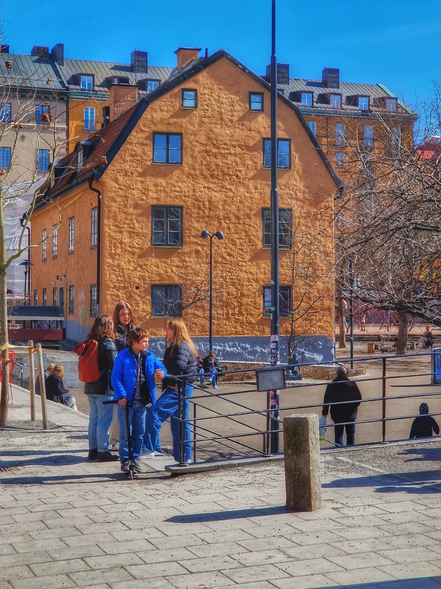 Grupp ungdomar vid orange byggnad med skyltar "förskola" och "skola" i fönstren. Gatubild