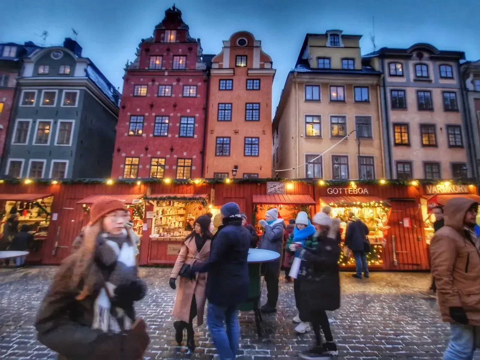 Människor vid julmarknad framför flerfärgade byggnader i Gamla stan