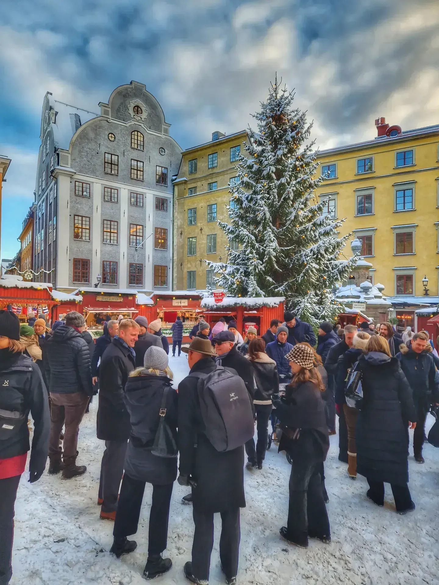 Snötäckt torg med folkmassa, julgran och röda marknadsstånd