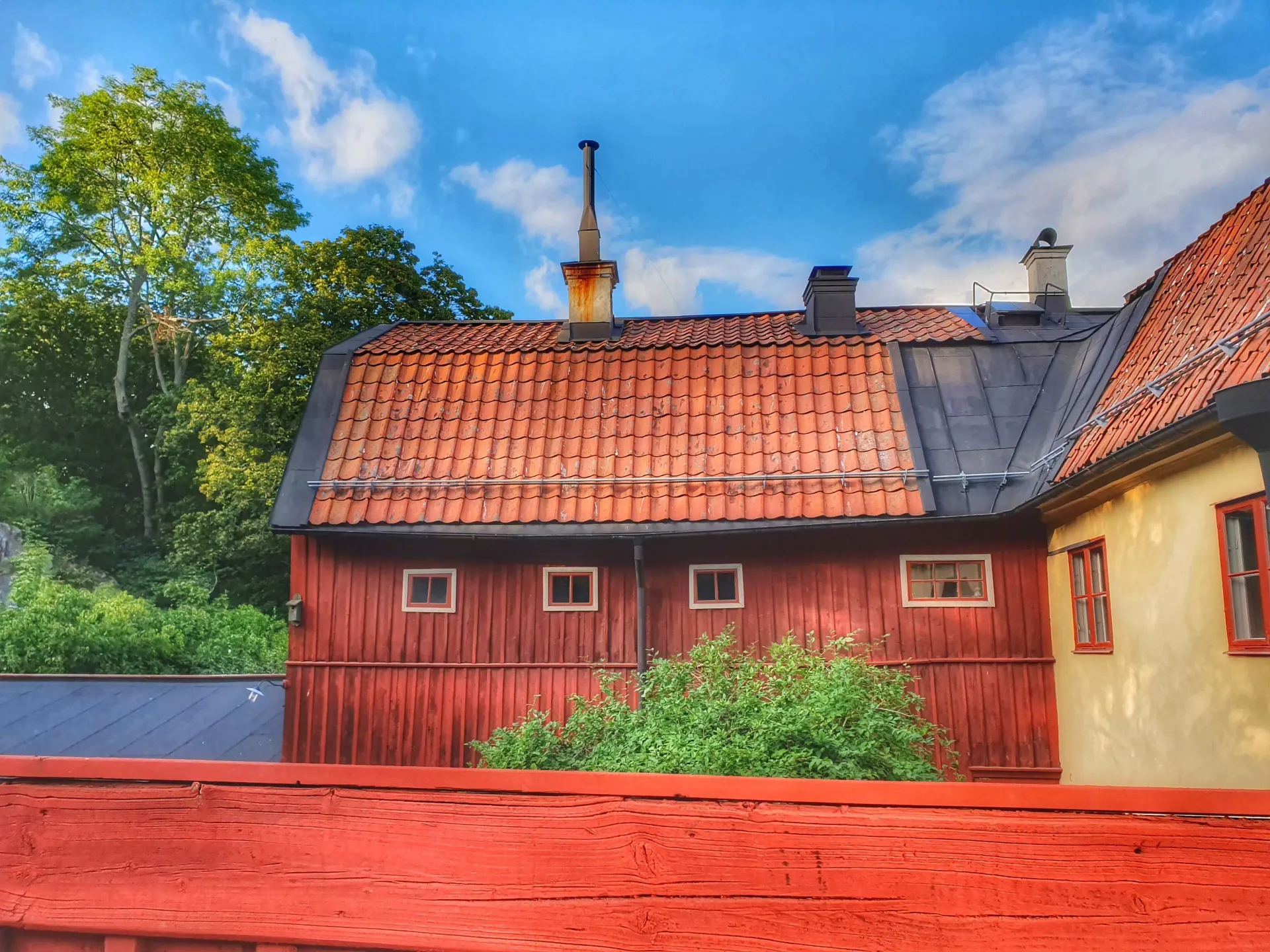 Rött plank framför röda och gula hus med tegeltak mot blå himmel