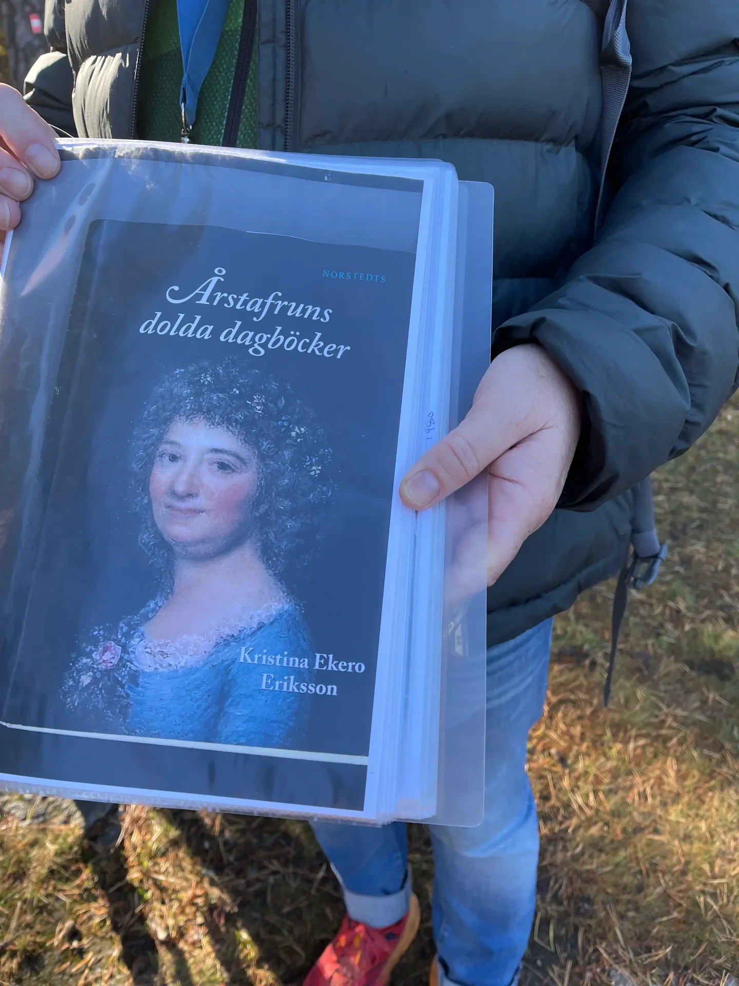 Person håller "Årstafruns dolda dagböcker". Porträtt av kvinna på omslaget