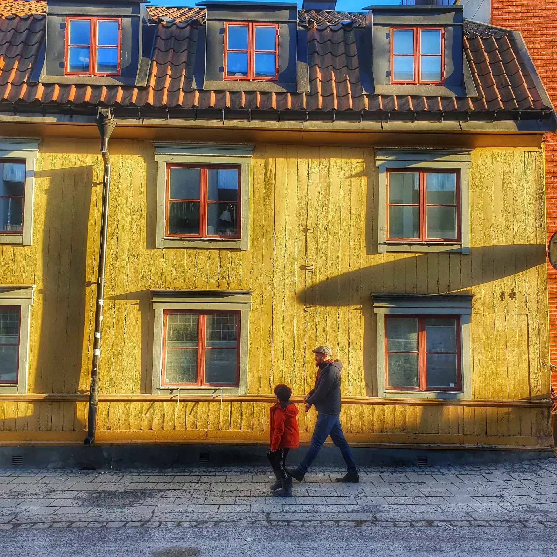 Personer går förbi gult hus med röda fönster