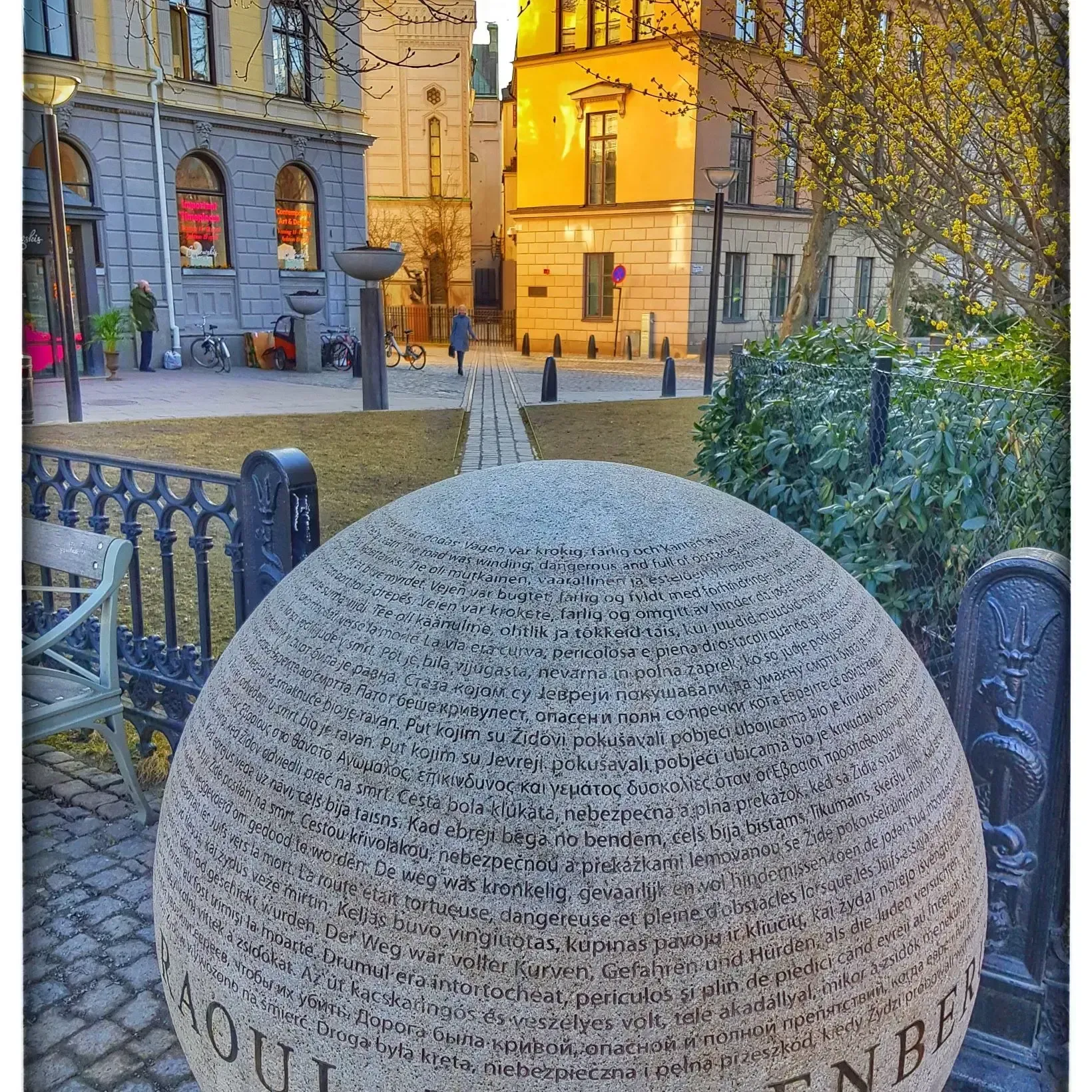 Stenklot med text i parkmiljö, troligen Ö i Stockholm. Byggnader och träd i bakgrunden