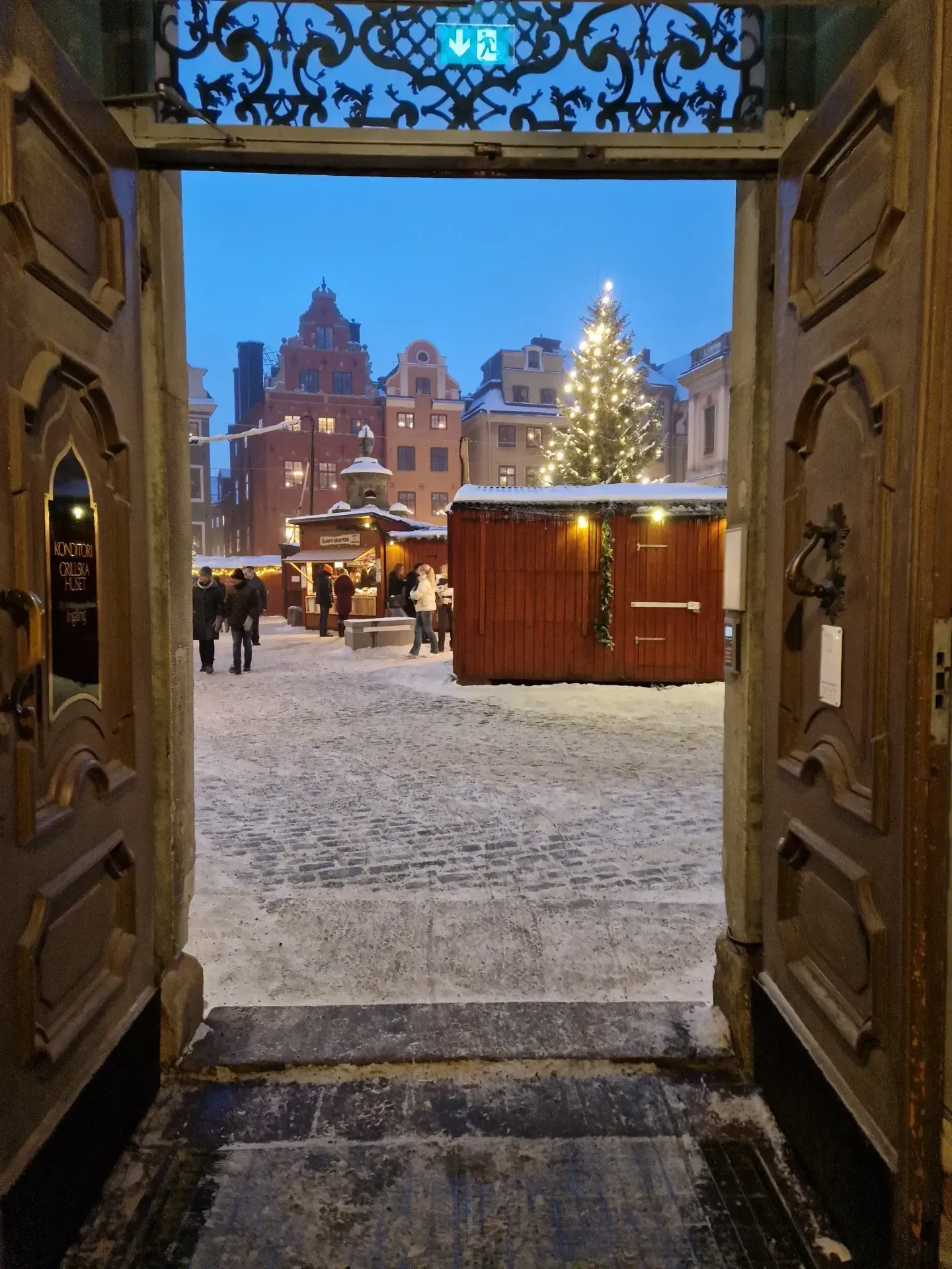 Utsikt genom öppen dörr mot torg med julgran och julmarknad