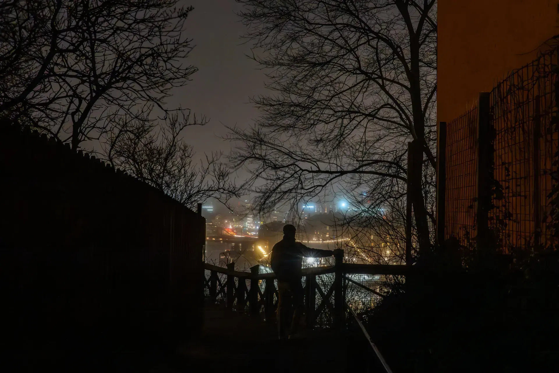 Silhuett av person som tittar ut över stad från Söders höjder nattetid