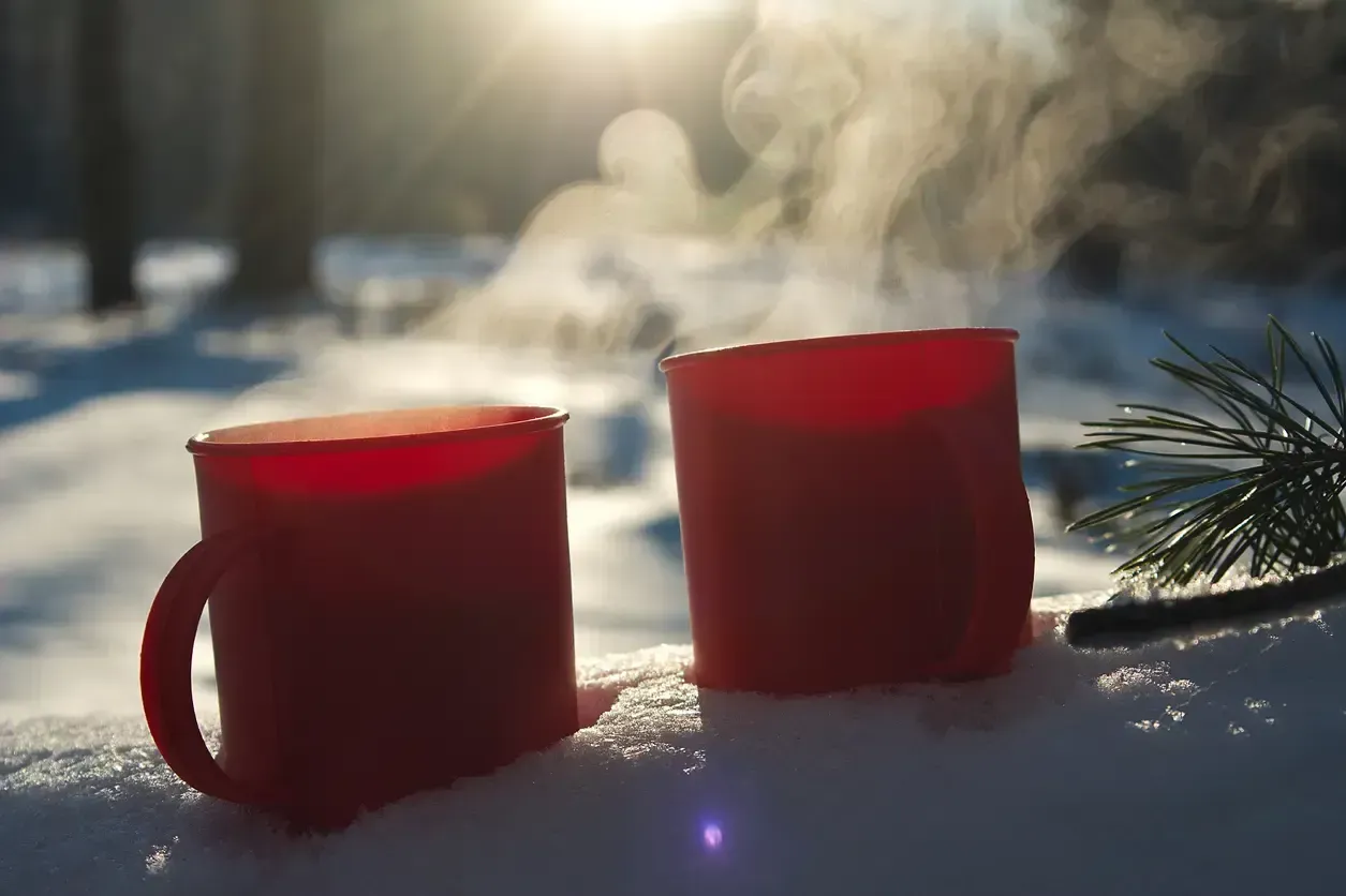 Två röda muggar med ånga i snö och solsken