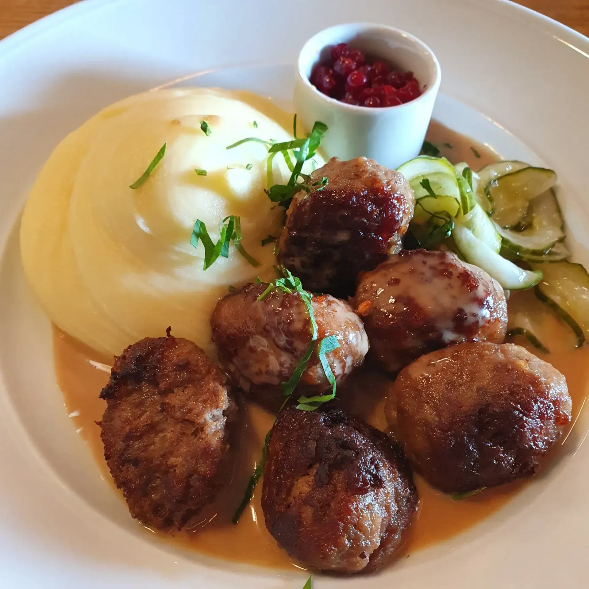 En tallrik med potatismos, sex köttbullar, inlagd gurka och en skål med lingonsylt