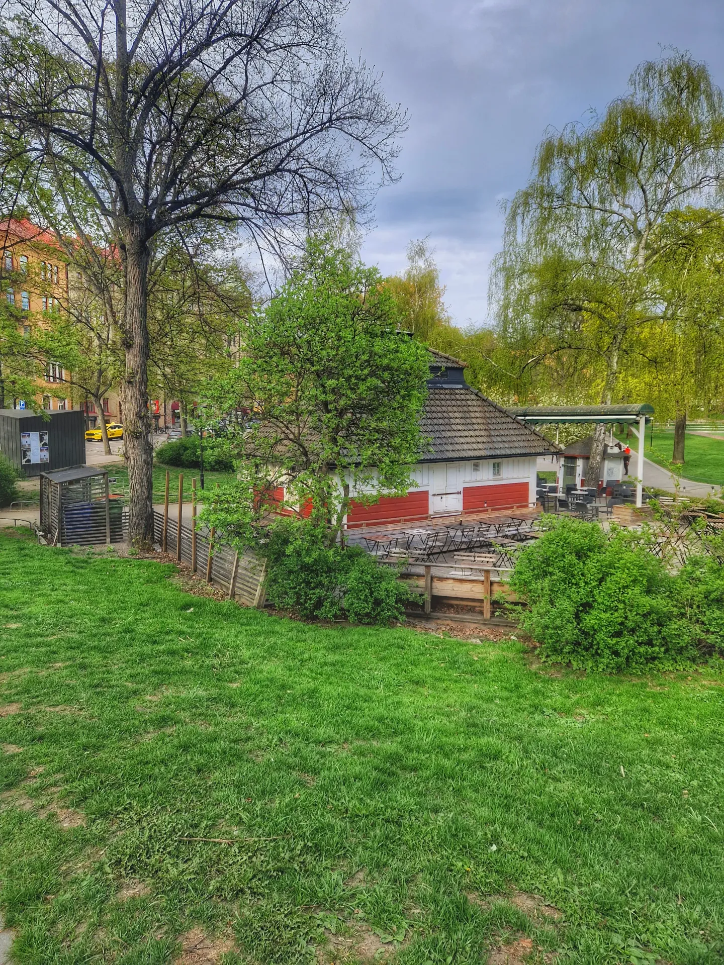 Gräsmatta, träd och en röd och vit byggnad med utomhusservering