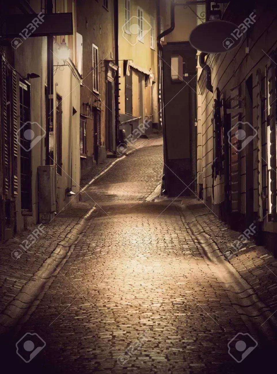Gata med kullersten mellan hus. Ljus fläckvis på gatan