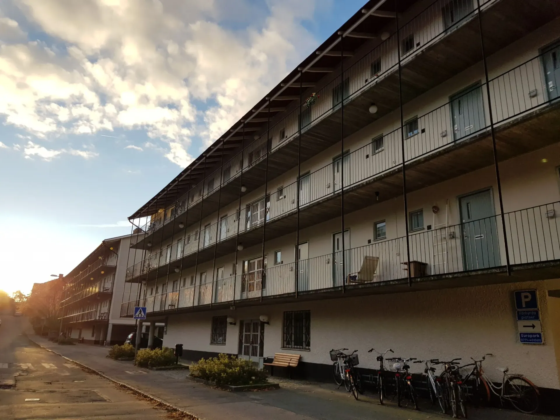 Flerfamiljshus med balkonger längs en gata med cyklar parkerade. Molnig himmel