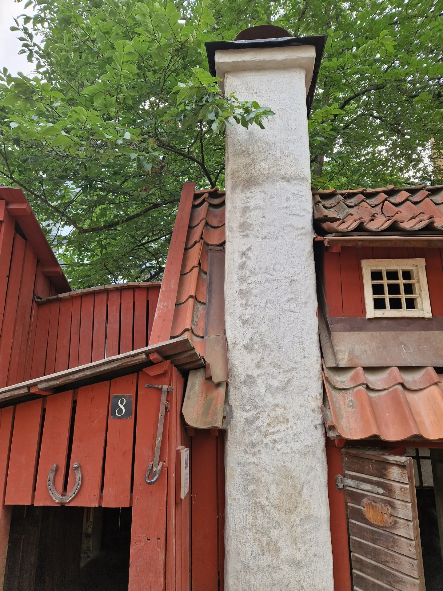Rött trähus med skorsten och tegeltak. Ett fönster och dörr syns. Hästsko på väggen