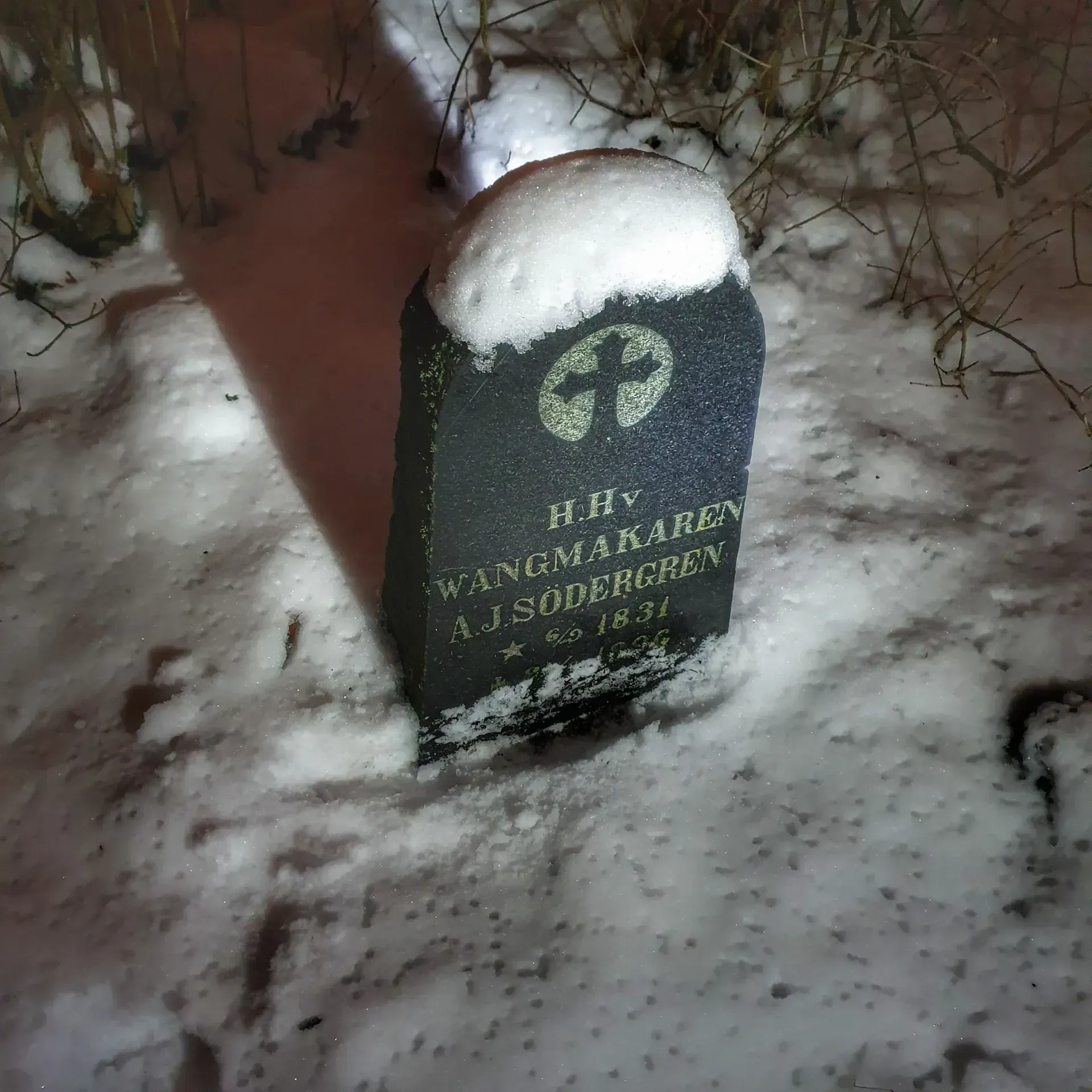Gravsten med texten "H.H.v WANGMAKAREN A.J. SÖDERGREN * 1831" delvis täckt med snö