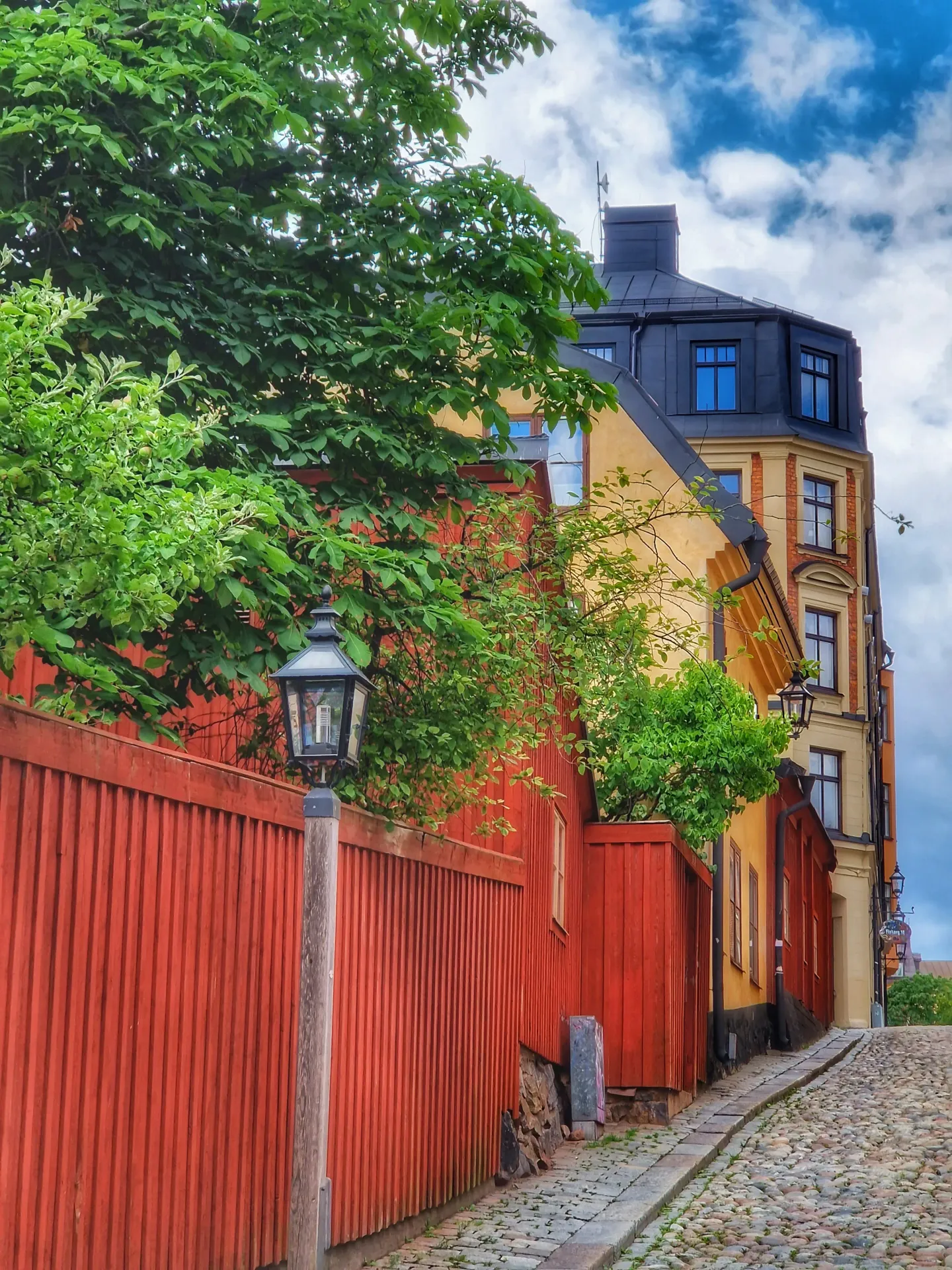 Gata med kullerstenar, rött staket, lampa och färgglada hus