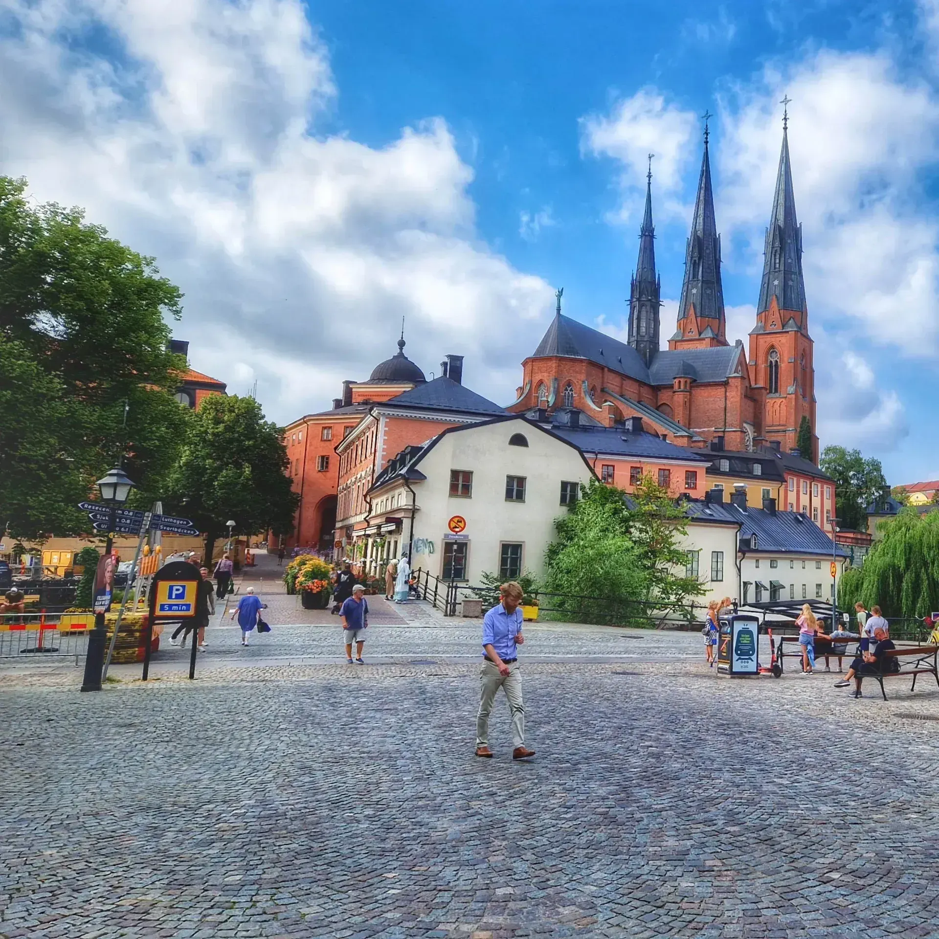 Uppsala Domkyrka syns bakom hus på kullerstensgata med folk. Stadsvandring Uppsala