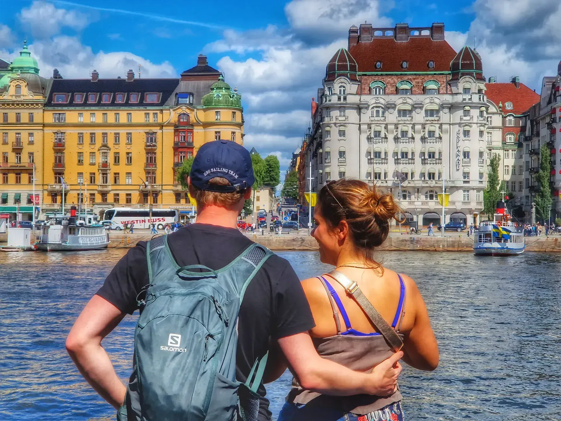 Ett par står vid vattnet och tittar mot Stockholm. Byggnader syns i bakgrunden