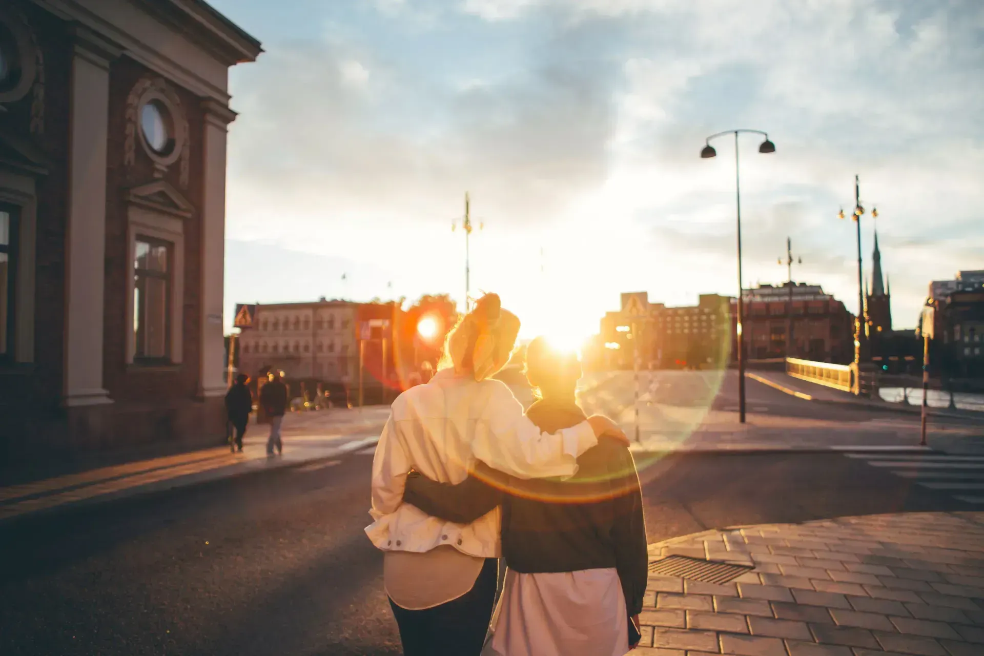 Två personer med armarna om varandra på gata med solnedgång i Stockholm
