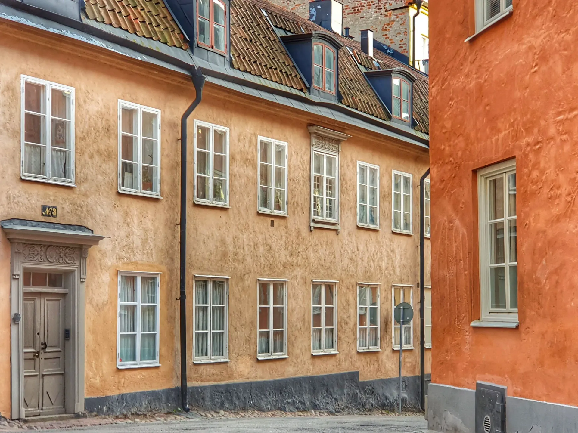 Fasader i ockra och orange med vita fönster och tegeltak