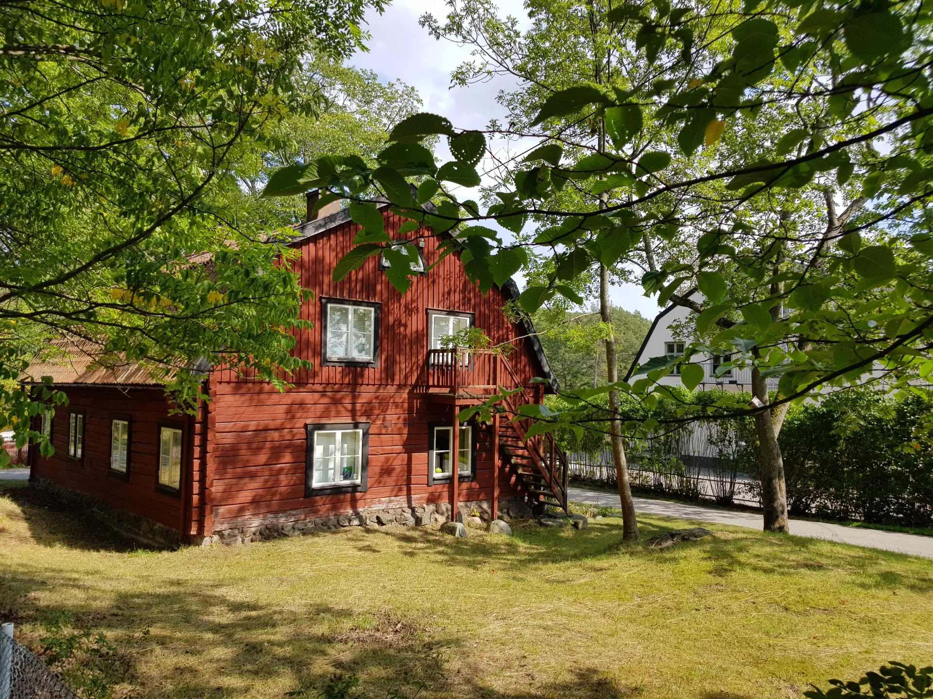 Rött trähus med vita fönster och en liten balkong. Grönska i förgrunden