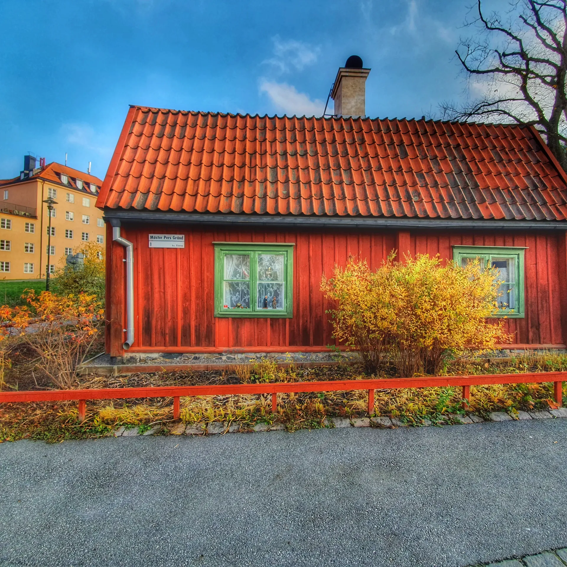 Rött trähus med tegelpannor, grönmålade fönster och en liten trädgård. Skylt: "Mäster Pers Gränd"