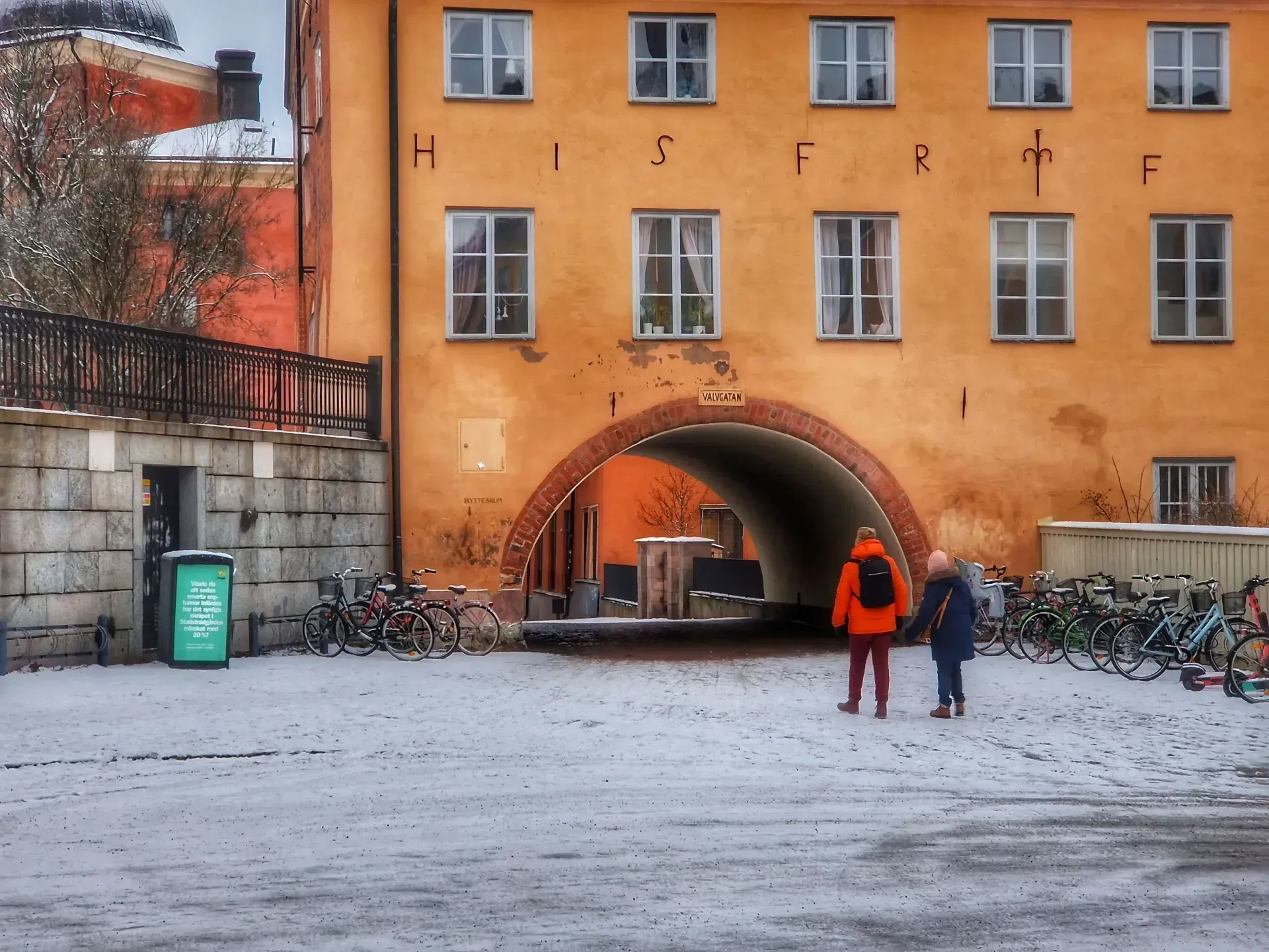 Två personer går mot en valvgång i Uppsala. Många cyklar syns. Snö på marken
