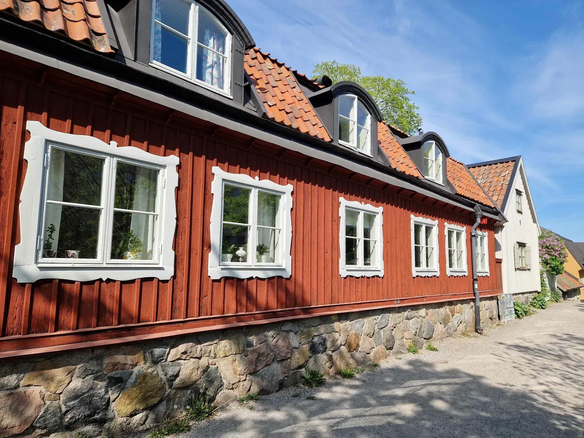 Rött trähus med vita fönster och tegeltak, stengrund. Blå himmel