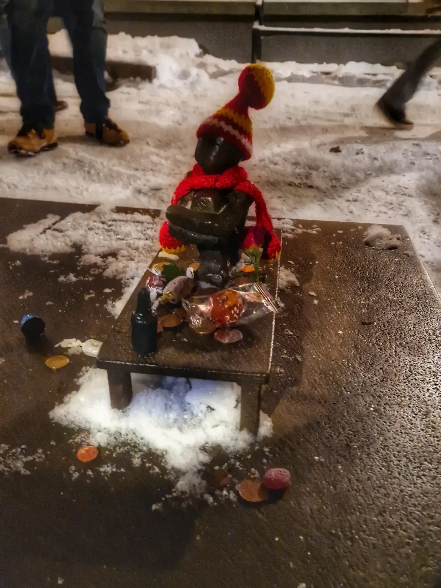 Staty med mössa och halsduk står på ett litet bord täckt med godis i snön