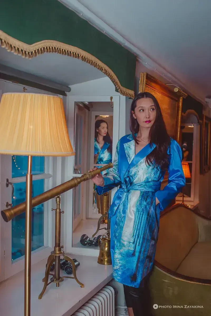 Kvinna i blå kimono vid fönster. Teleskop och lampa på fönsterbrädan. Spegelbild av kvinnan syns