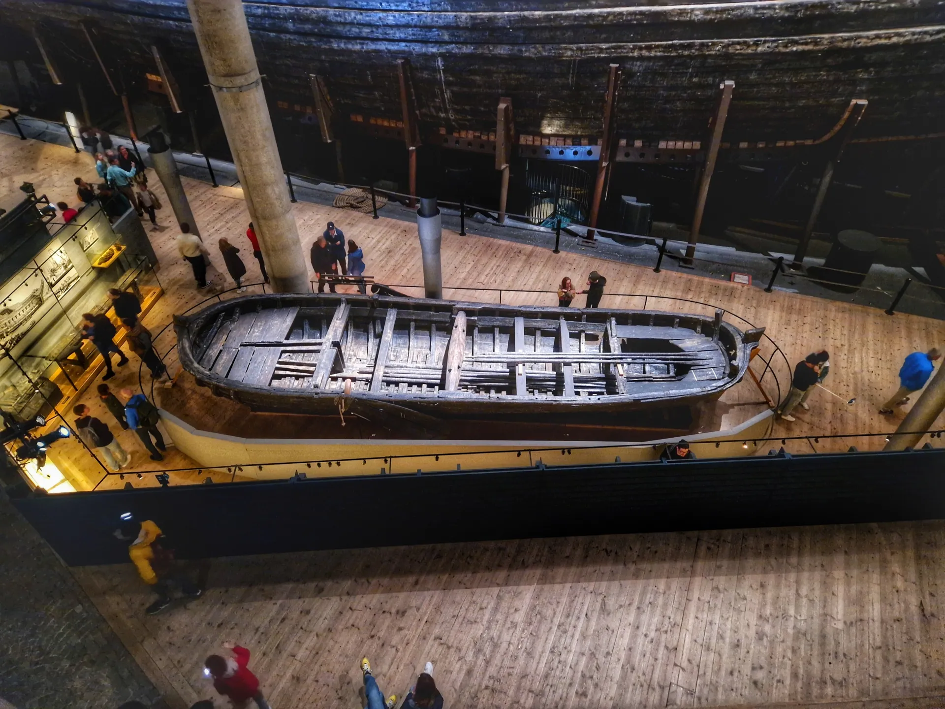 Inifrån ett museum med ett stort, mörkt skepp och en mindre träbåt. Besökare på trägolvet