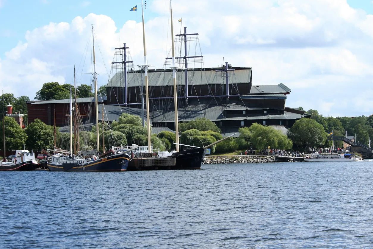 Stora segelfartyg vid kaj framför Vasamuseet och en folksamling vid vattnet, under delvis molnig himmel