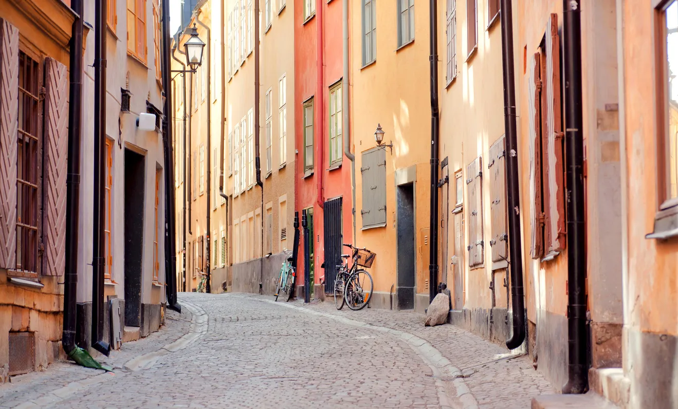 Smal kullerstensgata kantad av gamla färgglada hus med fönsterluckor. Två cyklar står parkerade